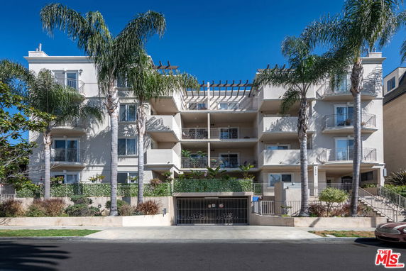 Front view of a multi-story building with balconies and palm trees.
