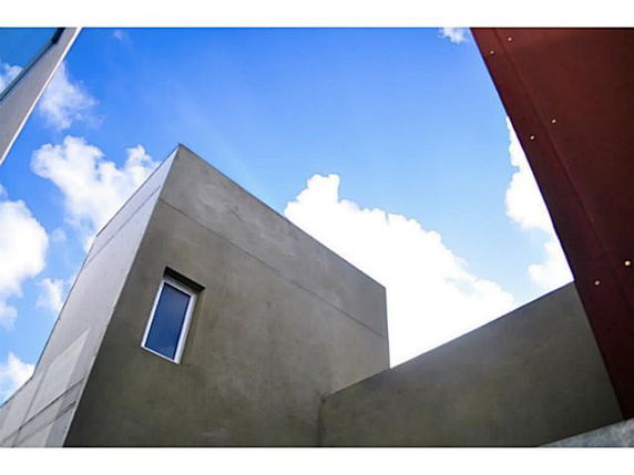 Modern building with a flat roof and a small window against a blue sky.