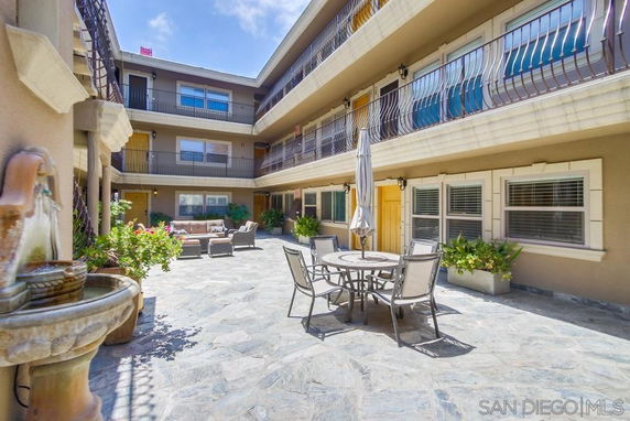 Open courtyard area with tables, chairs, and plants surrounded by a multi-story building.