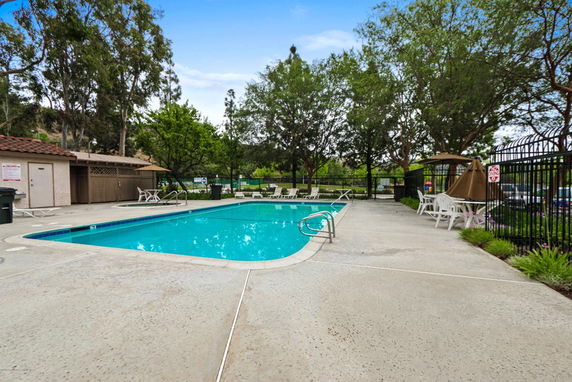 Outdoor swimming pool area with lounge chairs and trees.