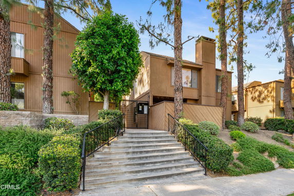 Front view of a multi-story building with wood paneling and large windows, surrounded by trees and greenery.