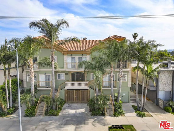 Front view of a two-story house with a tile roof and palm trees.