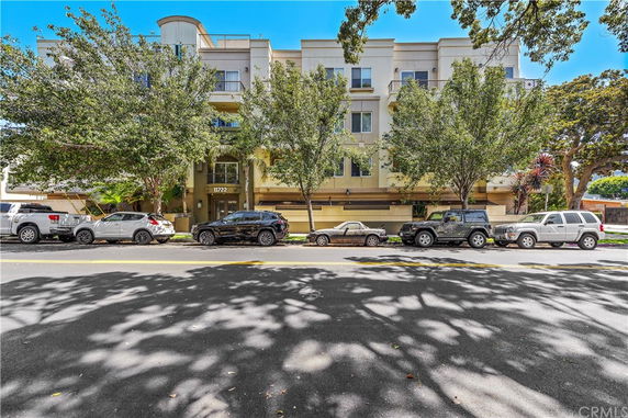 Front view of a multi-story apartment building with trees and parked cars in front.