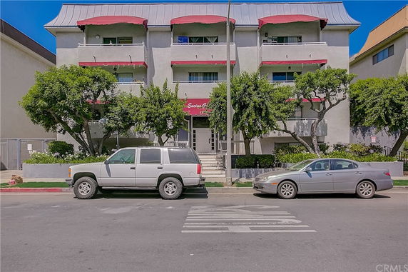 Front view of a multi-story residential building with red awnings and trees in front.