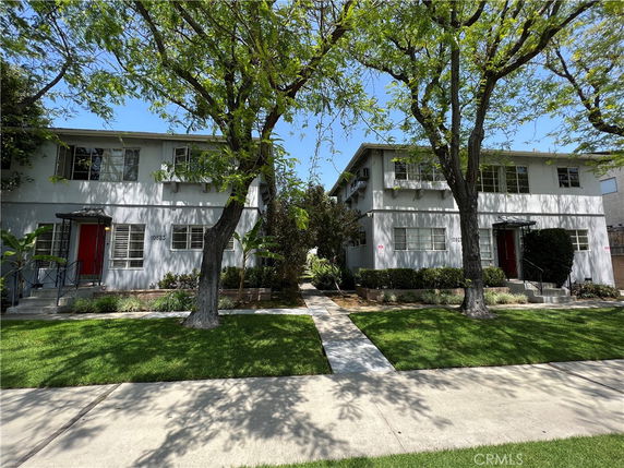 Front view of two-story residential buildings with red doors and surrounding trees.