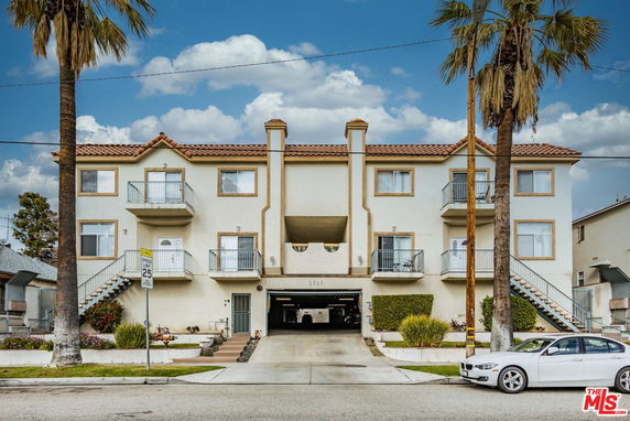 Front view of a multi-story apartment building with staircases on either side and a central driveway entrance.