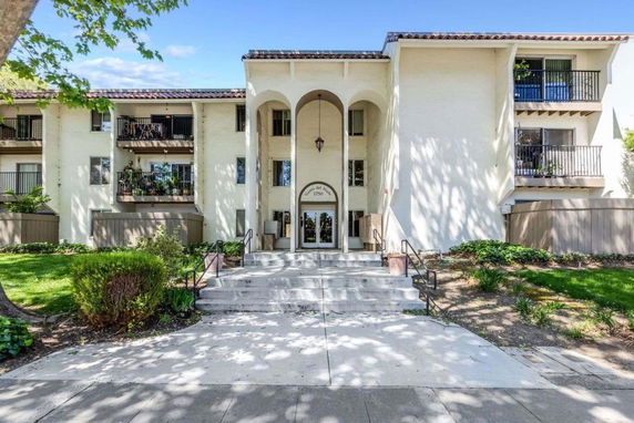 Front view of a multi-story residential building with balconies and an arched entrance.