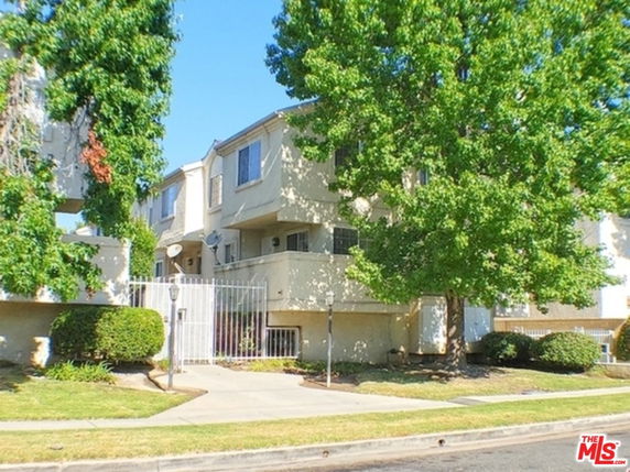 Front view of a multi-story residential building with trees and a gated entrance.