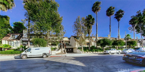 Front view of a multi-story residential building with trees and parked cars.
