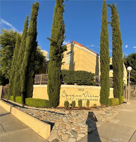 Front view of a residential condominium building with tall trees along the entrance.