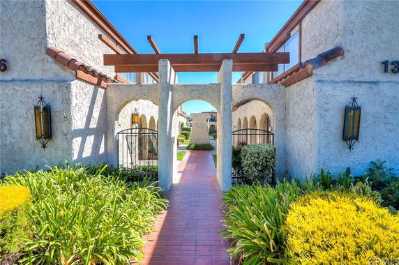 Front view of a building with arches and wooden beams, featuring a pathway leading through an archway.