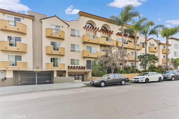 Front view of a multi-story residential building with balconies and a gated parking area.