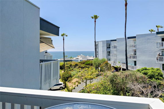 Ocean view from a balcony with multiple apartment buildings and palm trees.