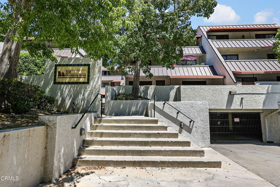 Front view of a multi-story building with balconies and a staircase leading up to the entrance.