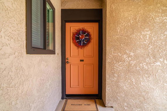 Front view of a house entrance with an orange door and a welcome mat.