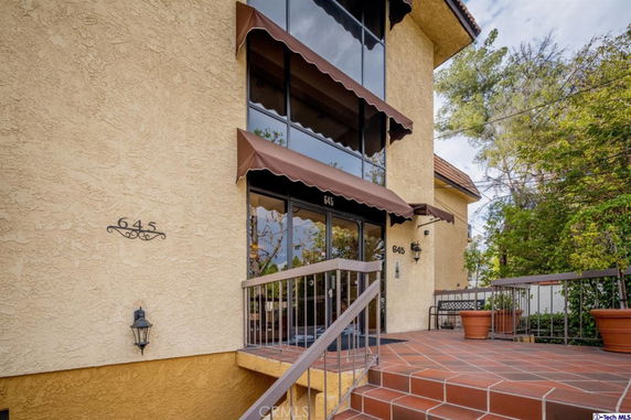 Front view of a beige multi-story building entrance with a tiled pathway leading to the door.