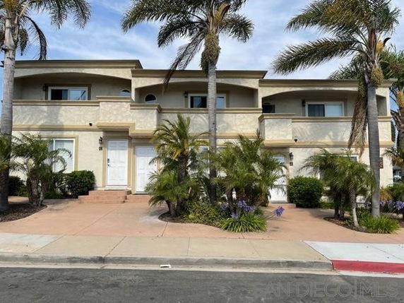 Front view of a two-story house with balconies and palm trees.