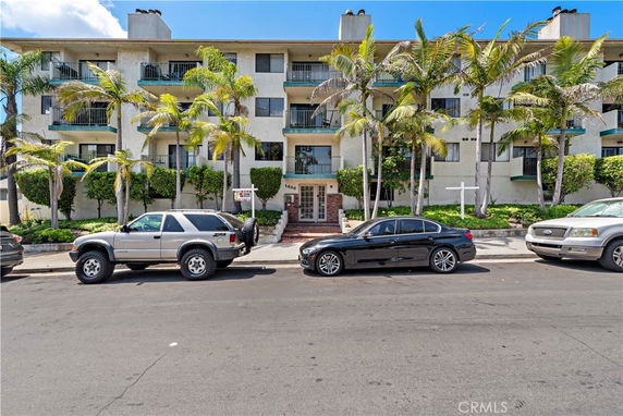 Front view of a multi-story apartment building with balconies and palm trees.
