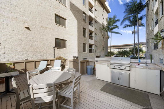 Outdoor area with dining table and barbecue grill; buildings in background.