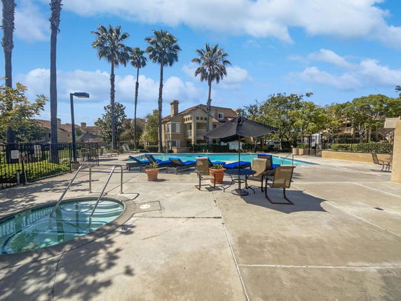 Swimming pool area with lounge chairs and an umbrella in front of a residential building.