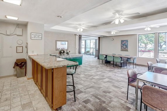 Interior view of a recreational area with tables and chairs, a small serving counter, and large windows.