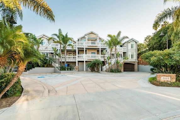 Front view of a multi-story house with balconies and palm trees.