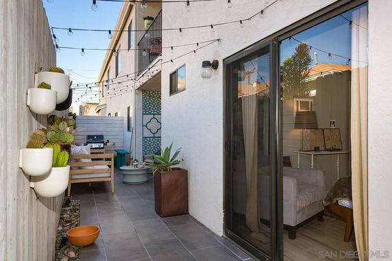 Narrow outdoor area with string lights and potted plants next to a building.