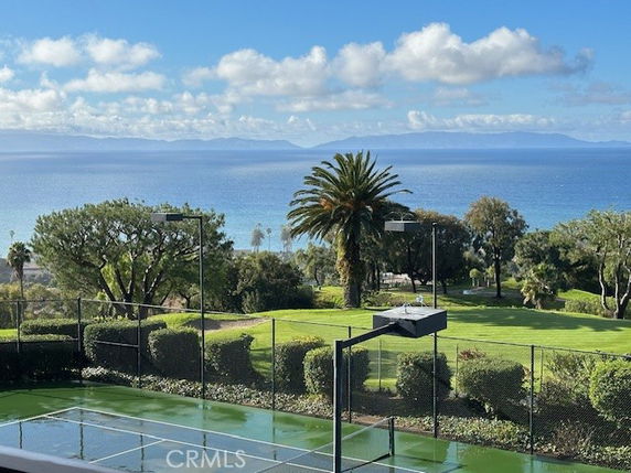 Panoramic view of a tennis court with ocean and landscape in the background.