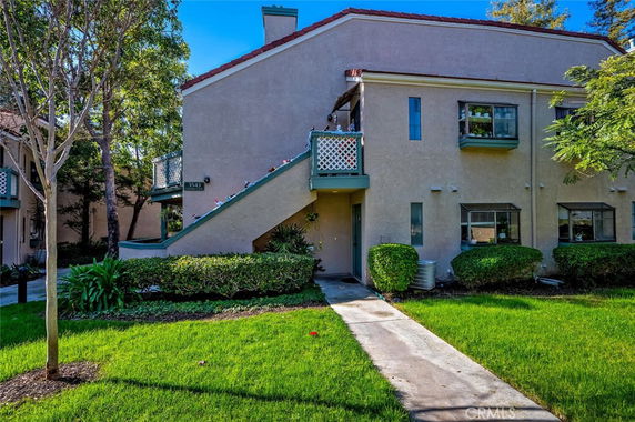 Front view of a two-story residential building with exterior stairs and green landscaping.