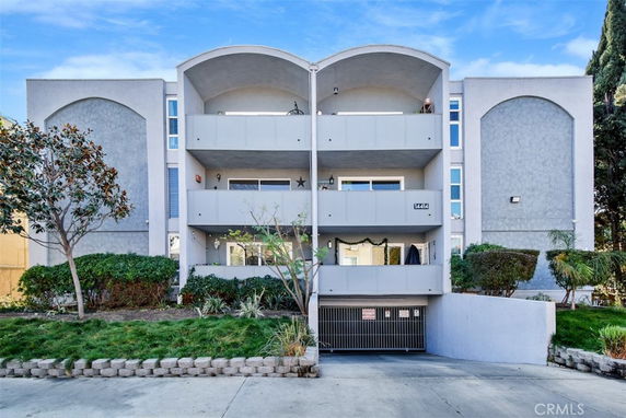 Front view of a multi-story apartment building with balconies and a gated entrance.