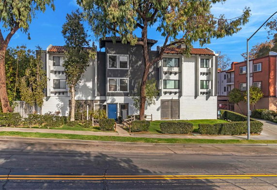 Front view of a multi-story residential building with trees and a walkway.