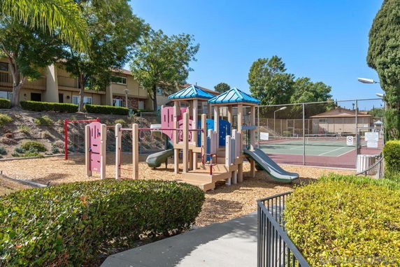 Outdoor playground with a slide and climbing structure near a tennis court.