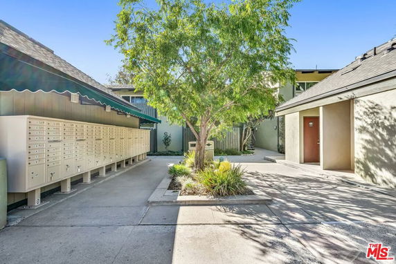 Outdoor view featuring multiple mailbox units under an awning next to a tree.