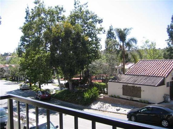 View from a building balcony overlooking a street with trees and nearby houses.