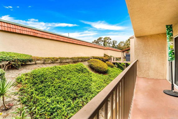 View from a building's balcony overlooking manicured bushes and a wall.