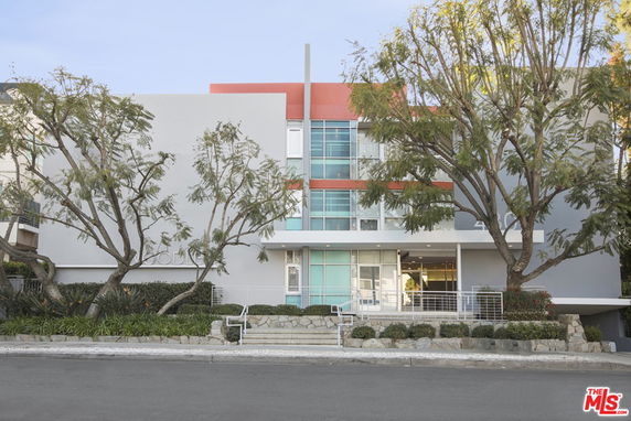 Front view of a modern multi-story building with large windows and a mix of grey and red colors.