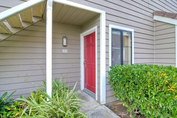 Front view of a residential building with a red door and grey siding.