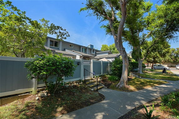 Front view of a two-story house with a blue fence and surrounding trees.