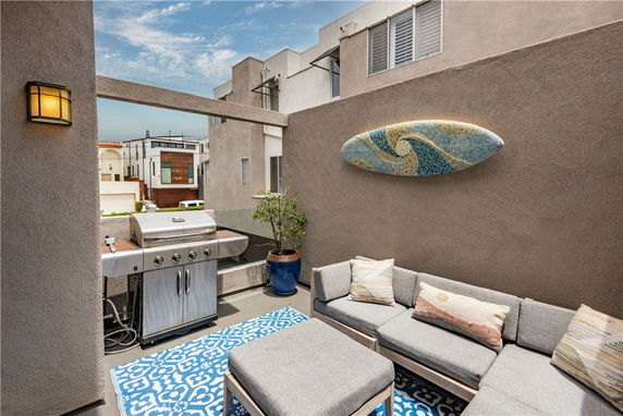 Rooftop patio area with a couch, grill, and decorative wall piece.
