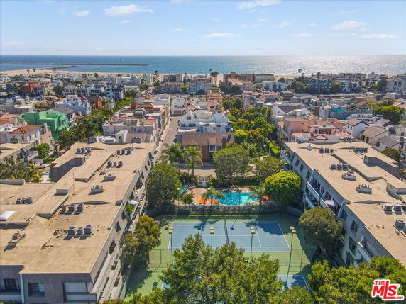 Panoramic view of a coastal neighborhood with tennis courts, buildings, and the ocean in the background.