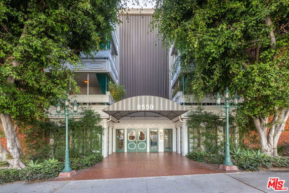 Front view of a multi-story building entrance with a canopy and greenery.