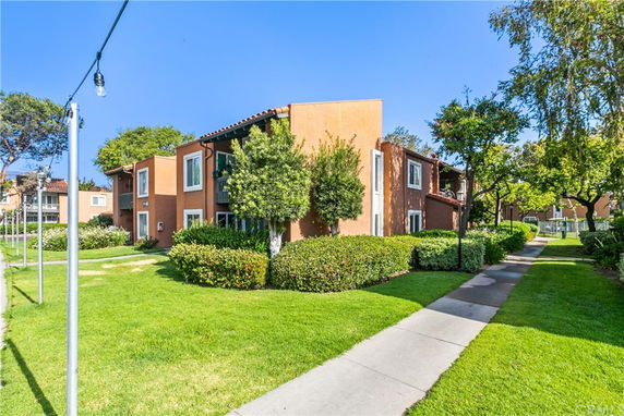 Front view of a two-story brown residential building with surrounding greenery.