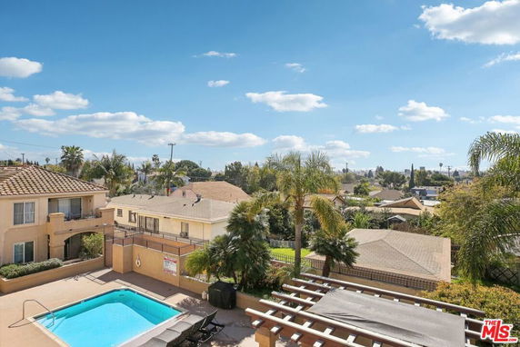 Panoramic view from a building overlooking a swimming pool and surrounding residential area under a blue sky.