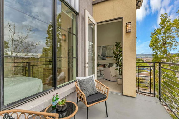 View of open balcony with chairs and table, overlooking a tree-filled neighborhood with hills in the background.