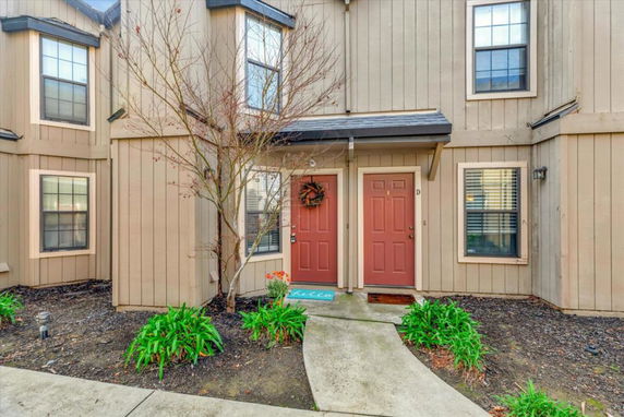 Front view of a two-story townhouse with tan siding and red doors.