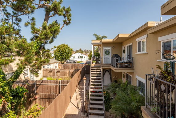 View of a multi-story building with external staircase and a fenced area in a residential neighborhood.