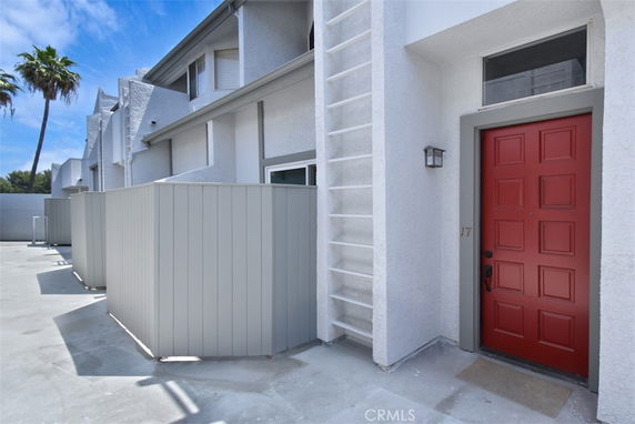 Front view of a modern multi-story townhouse with a red front door and patio area.
