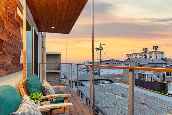 View from a balcony overlooking rooftops and the ocean at sunset.