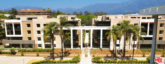 Front view of a modern multi-story residential building with palm trees and mountains in the background.