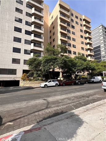 Front view of a multi-story apartment building with balconies and trees in front.